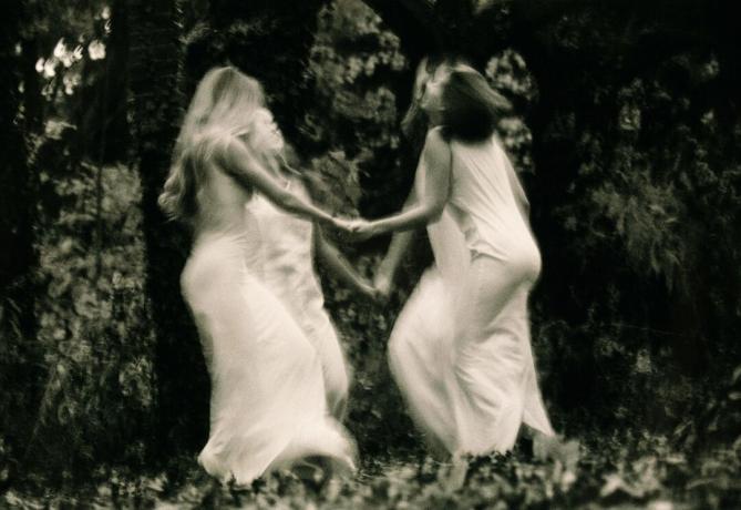 Neljä nuorta naista tanssii metsässä, kädestä (mustavalkoinen, sumea liike)