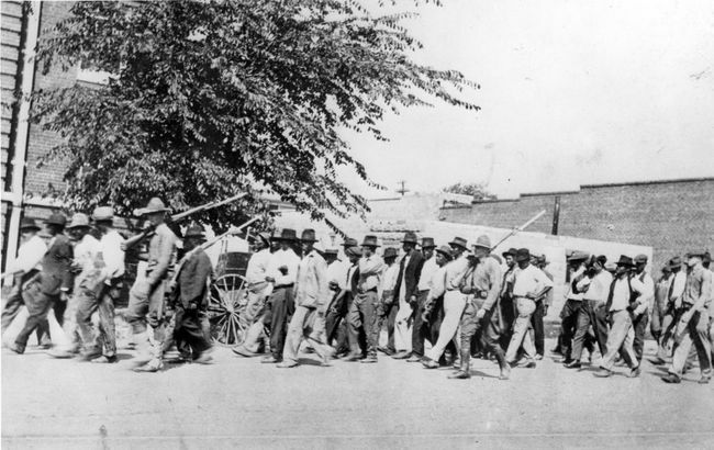 Joukko kansalliskaartin joukkoja, jotka kantavat pistimellä varustettuja kivääreitä, saattoivat aseettomia mustia miehiä pidätyskeskukseen Tulsa Race Massacren jälkeen, Tulsa, Oklahoma, kesäkuu 1921.