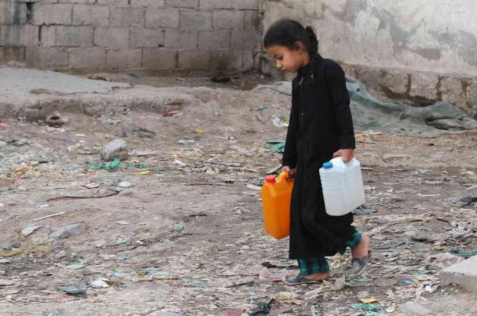 Pieni tyttö kantaa hyväntekeväisyyspumpusta puhtaalla vedellä täytettyjä kankeria jatkuvan puhtaan veden kriisin aikana Jemenissä