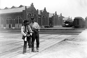 Kaksi palvelumiestä seisoo Pullman-rakennuksen vieressä ja kouluttaa lukittujen aseiden ja juomapullon autoja vuoden 1894 Chicagon Pullman-lakon aikana