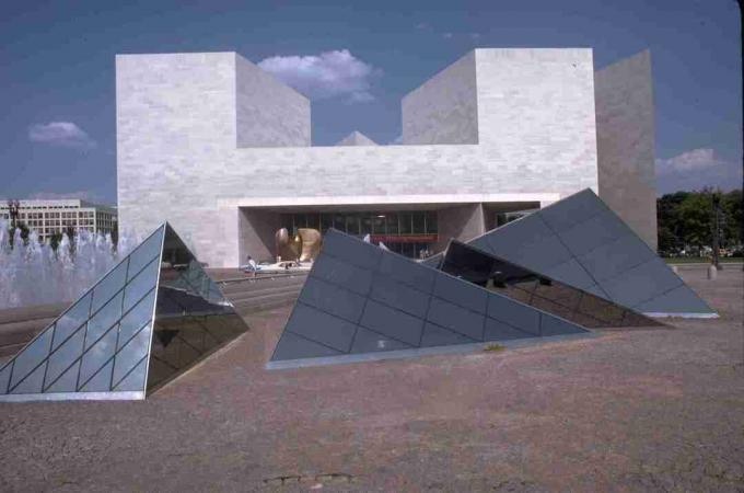 moderni valkoinen kivirakennus taustalla ja lasipyramidit kentällä etualalla