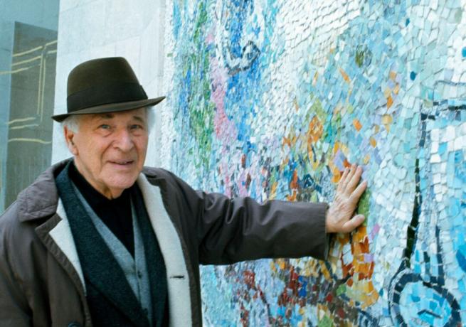 Taiteilija Marc Chagall hatulla painaa kättään seinää vasten, sinisillä mosaiikkikuvioilla.