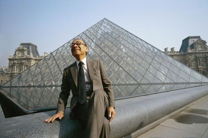 Kiinalainen mies puku istuu suuren lasipyramidin edessä