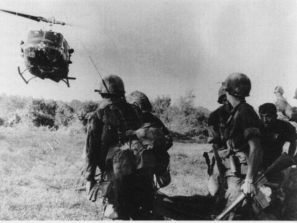 UH-1 Huey -helikopteri laskeutuu lähellä sotilasryhmää.