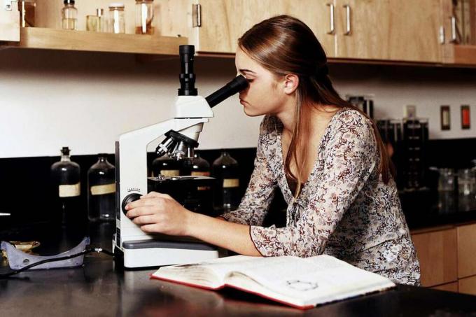 Teini-ikäinen tyttö (14-16) mikroskoopeilla tiedelaboratorion luokassa