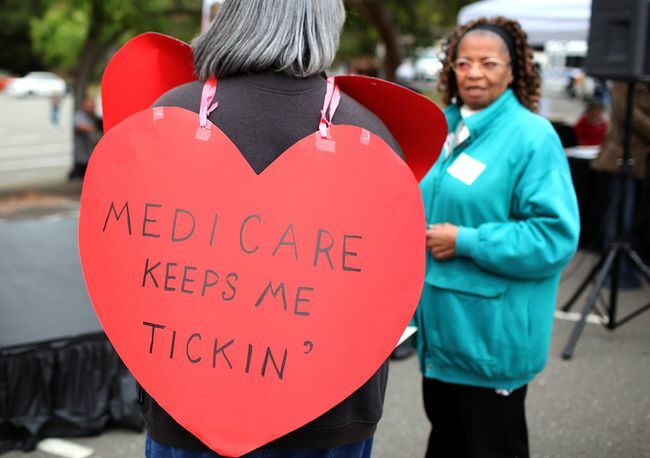 Nainen, jolla on sydämenmuotoinen kyltti, jossa lukee " Medicare Keeps Me Ticking"