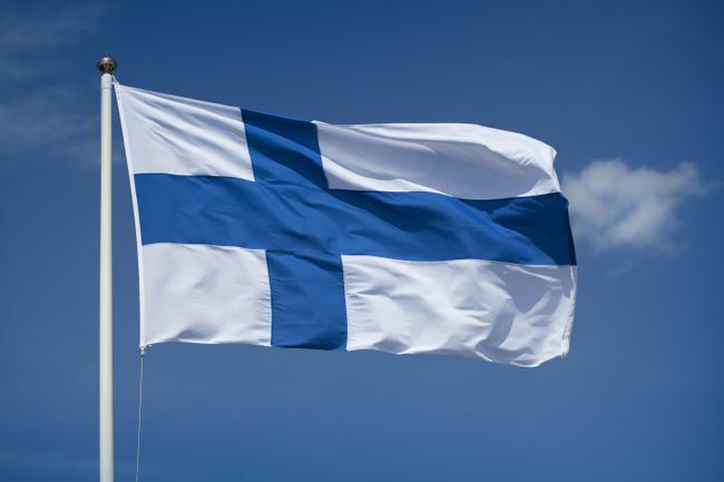 Nostettu Suomen lippu sinisellä taivaalla taustalla