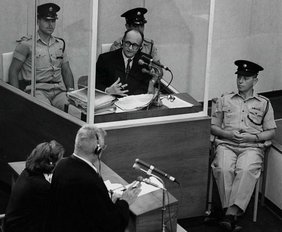 Natsien sotarikollinen Adolph Eichmann seisoo suojaavassa lasikaapissa, jota Israelin poliisi reunustaa 22. kesäkuuta 1961 Jerusalemissa pidetyn oikeudenkäynnin aikana.